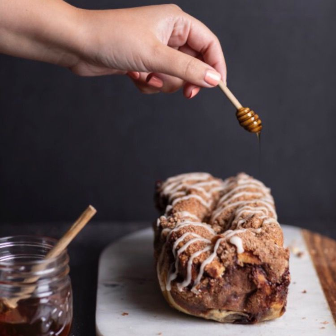 Honey being drizzled over a loaf of bread with a honey dipper on a dark background
